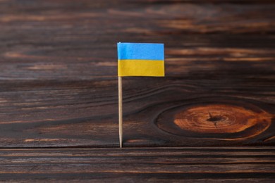 Photo of Small paper flag of Ukraine on wooden table, closeup