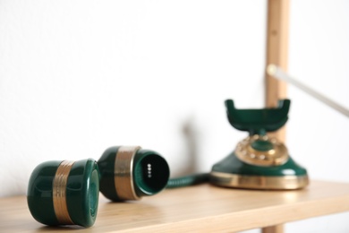 Photo of Handset and green vintage corded phone on wooden shelf near white wall, closeup