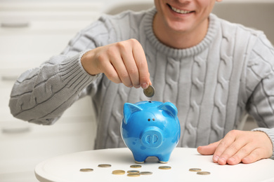 Photo of Man putting coin into piggy bank at white table, closeup