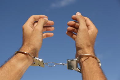 Photo of Man in handcuffs against blue sky outdoors, closeup