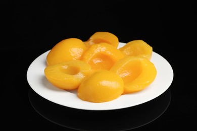 Photo of Plate with canned peach halves on black background