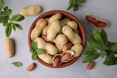 Photo of Fresh unpeeled peanuts in bowl and leaves on grey table, flat lay