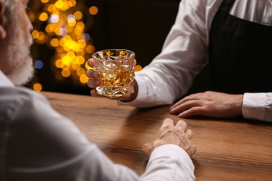 Photo of Bartender giving glass of whiskey to customer at bar counter, closeup