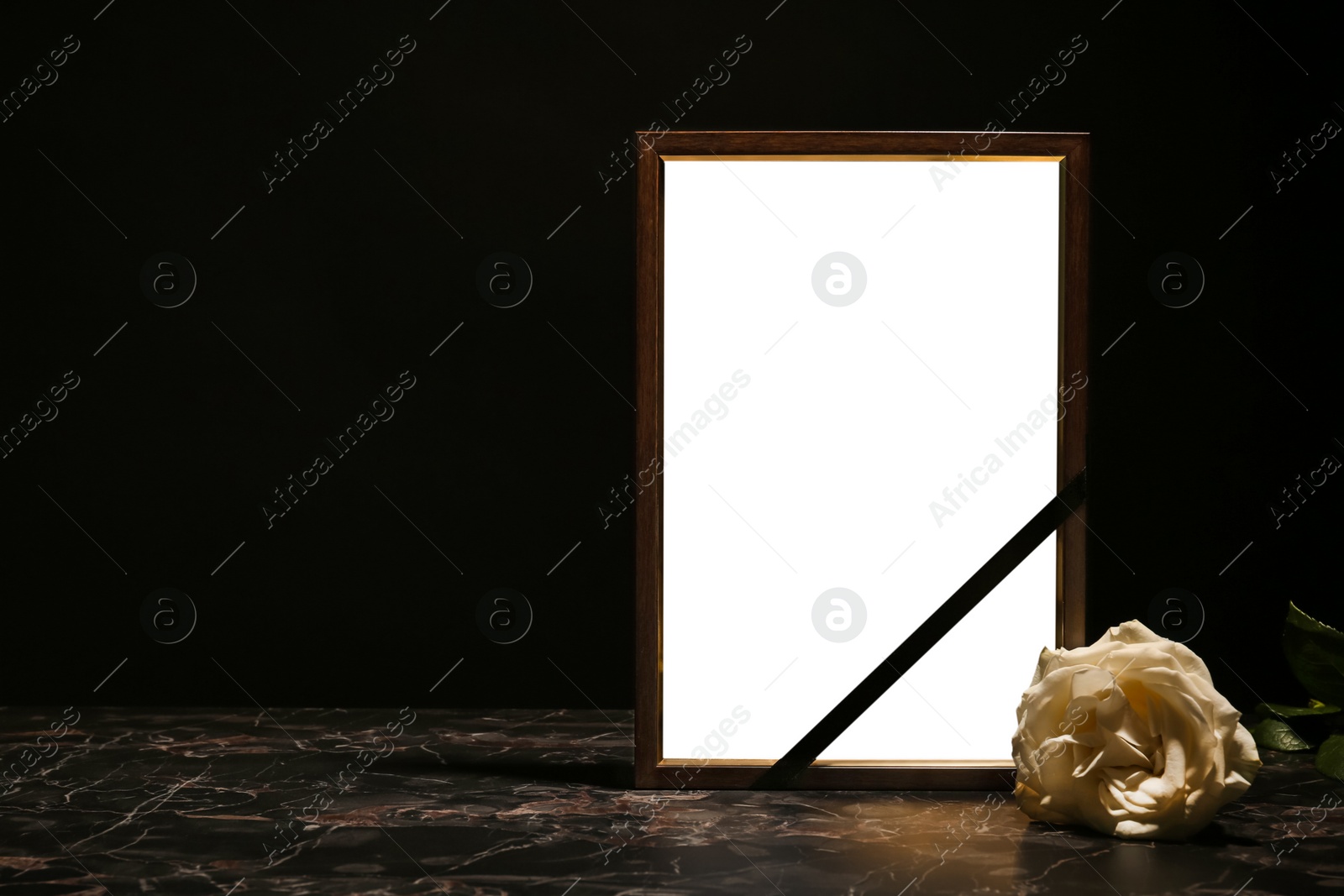 Photo of Empty frame with black ribbon and rose on table. Funeral symbol