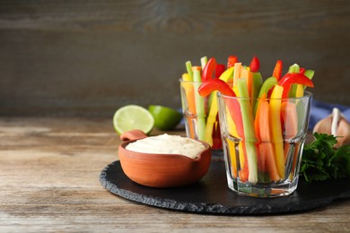 Photo of Fresh raw vegetable sticks and sauce on wooden table, space for text
