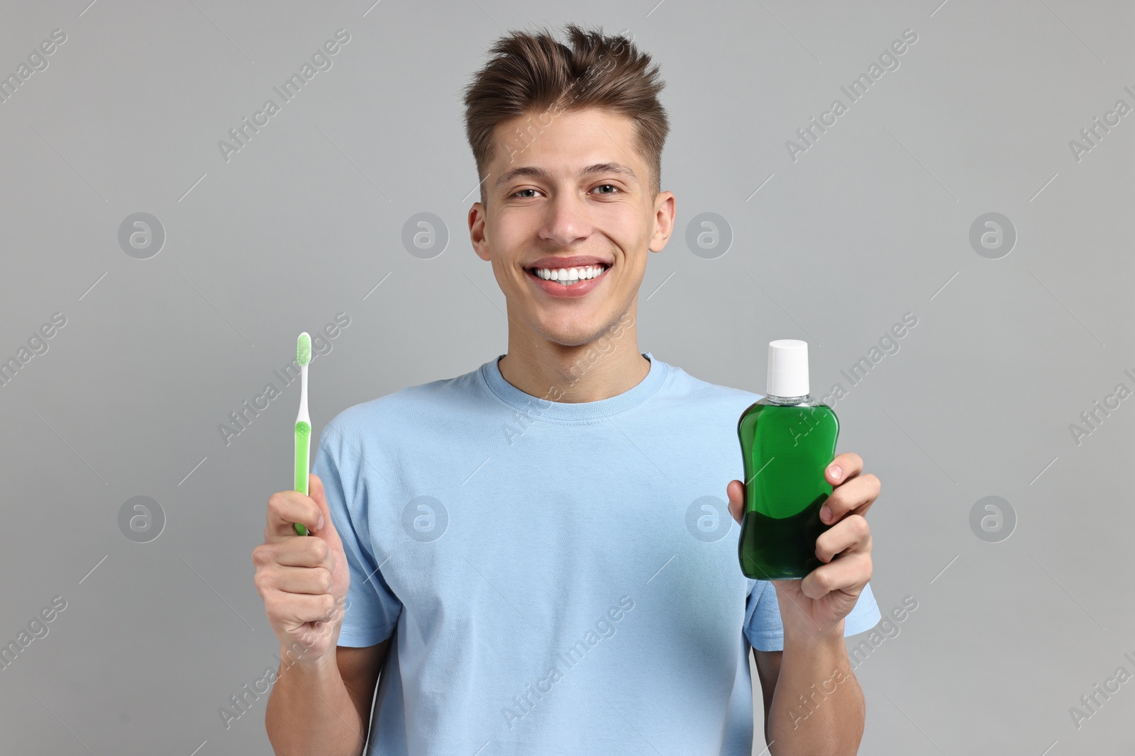 Photo of Young man with mouthwash and toothbrush on light grey background