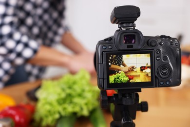 Photo of Food blogger cooking while recording video in kitchen, focus on camera