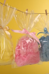 Photo of Packaged sweet cotton candies hanging on clothesline against yellow background
