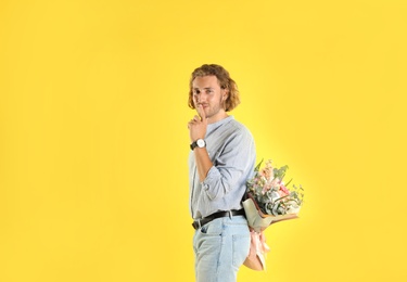 Photo of Young handsome man hiding beautiful flower bouquet behind his back on yellow background