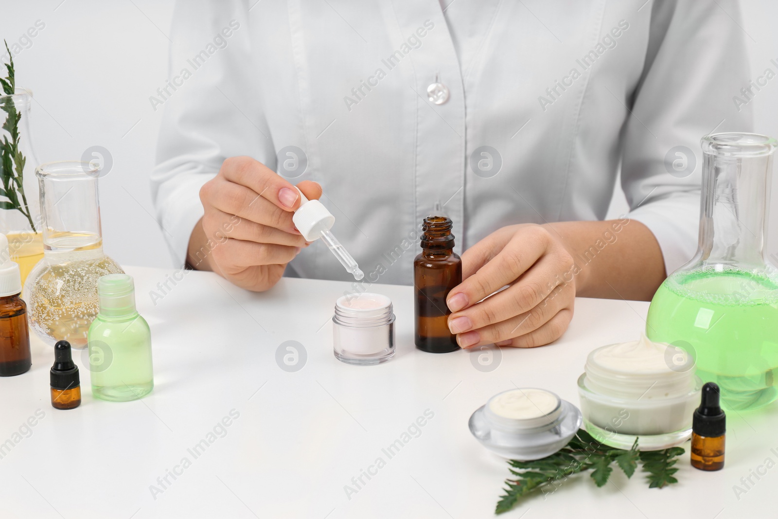 Photo of Female dermatologist creating skin care product at table, closeup