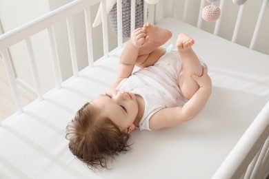 Photo of Cute little baby lying in comfortable crib at home