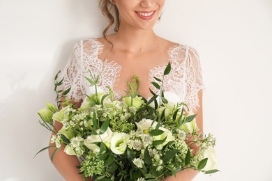 Photo of Young bride wearing wedding dress with beautiful bouquet on light background, closeup