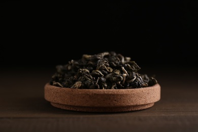 Photo of Dried green tea leaves in cork bowl on wooden table, closeup