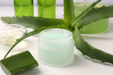 Photo of Jar of cosmetic gel and aloe vera leaves on white wooden table, closeup