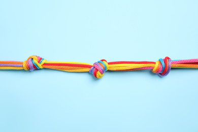 Photo of Colorful ropes tied together on light blue background, top view. Unity concept