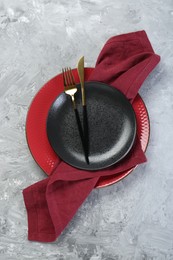 Clean plates, cutlery and napkin on gray textured table, top view