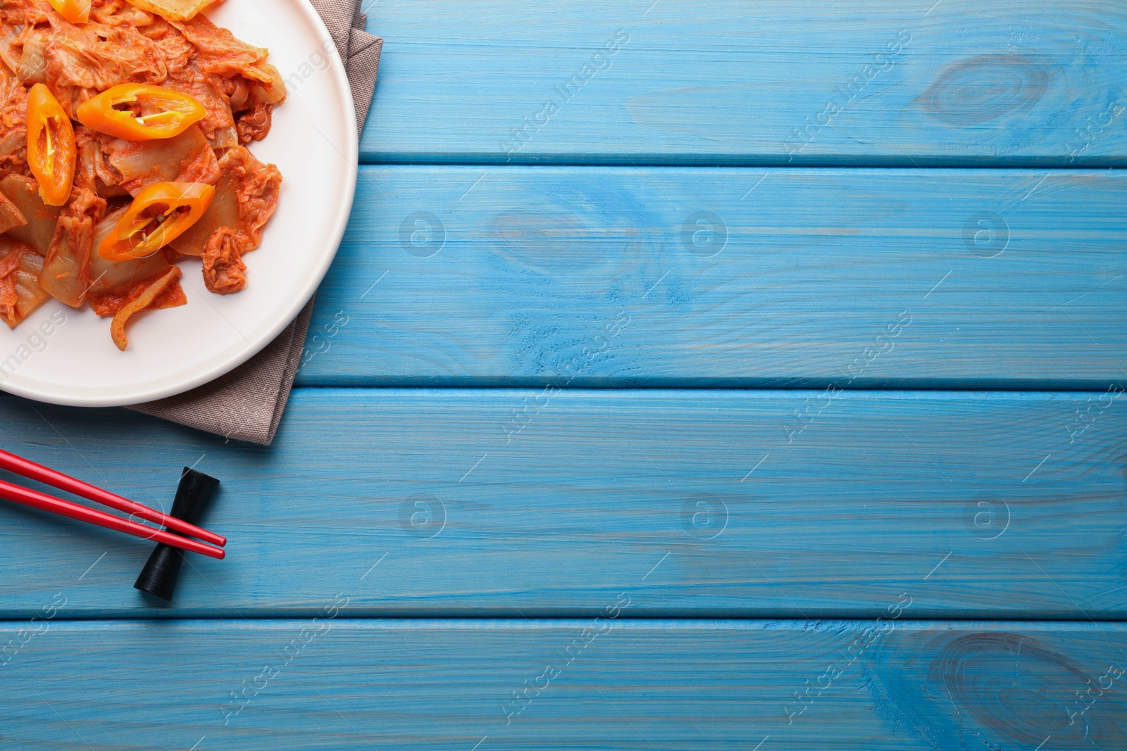 Photo of Plate of spicy cabbage kimchi with chili pepper and chopsticks on light blue wooden table, flat lay. Space for text