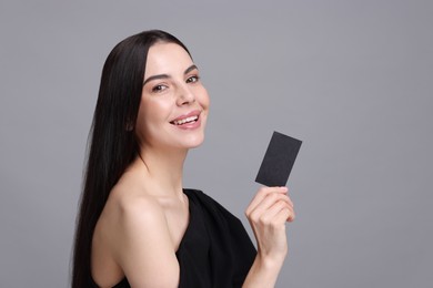 Photo of Happy woman holding blank business card on grey background. Space for text