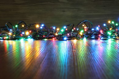 Photo of Beautiful colorful Christmas lights on wooden table. Space for text