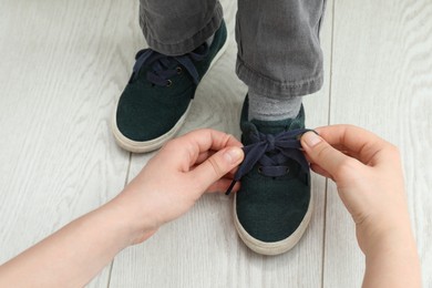 Photo of Mother helping son to tie shoe laces at home, closeup