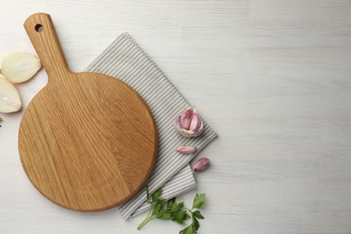 Photo of Cutting board, parsley, garlic and onion on white wooden table, flat lay. Space for text