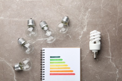 Flat lay composition with energy efficiency rating chart and light bulbs on marble background