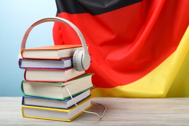 Photo of Learning foreign language. Different books and headphones on wooden table near flag of Germany, space for text