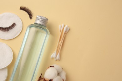Photo of Bottle of makeup remover, cotton flower, pads, swabs and false eyelashes on yellow background, flat lay. Space for text