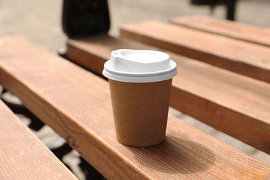 Photo of Takeaway paper cup with hot coffee on wooden bench outdoors