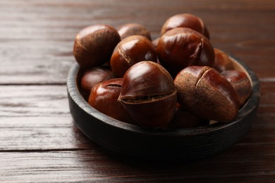 Photo of Roasted edible sweet chestnuts on wooden table, closeup
