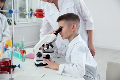 Photo of Schoolboy looking through microscope at table in chemistry class