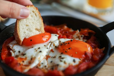 Photo of Woman dipping piece of bread into egg yolk, closeup. Eating tasty Shakshouka