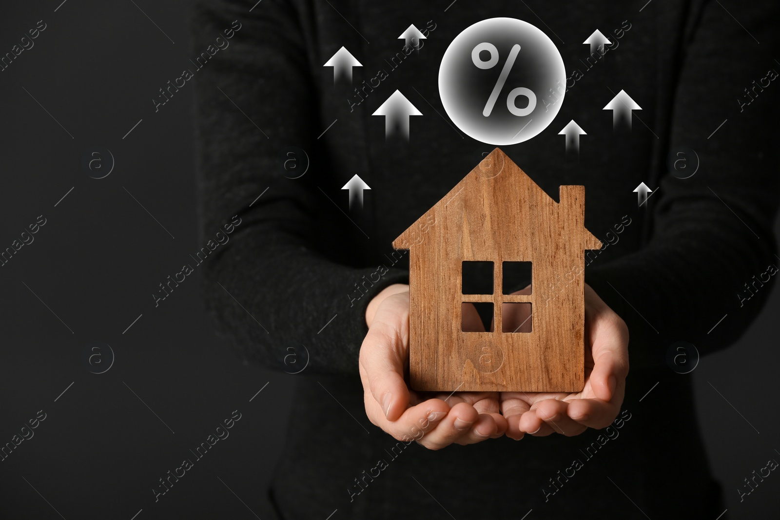Mortgage rate rising illustrated by upward arrows and percent sign. Woman with wooden house on dark background, closeup Image of Mortgage rate rising illustrated by upward arrows and percent sign. Woman with wooden house on dark background, closeup