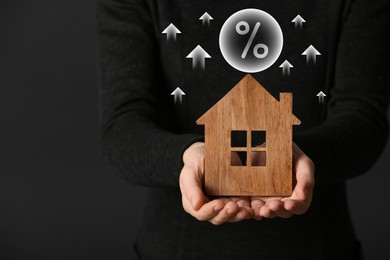 Image of Mortgage rate rising illustrated by upward arrows and percent sign. Woman with wooden house on dark background, closeup
