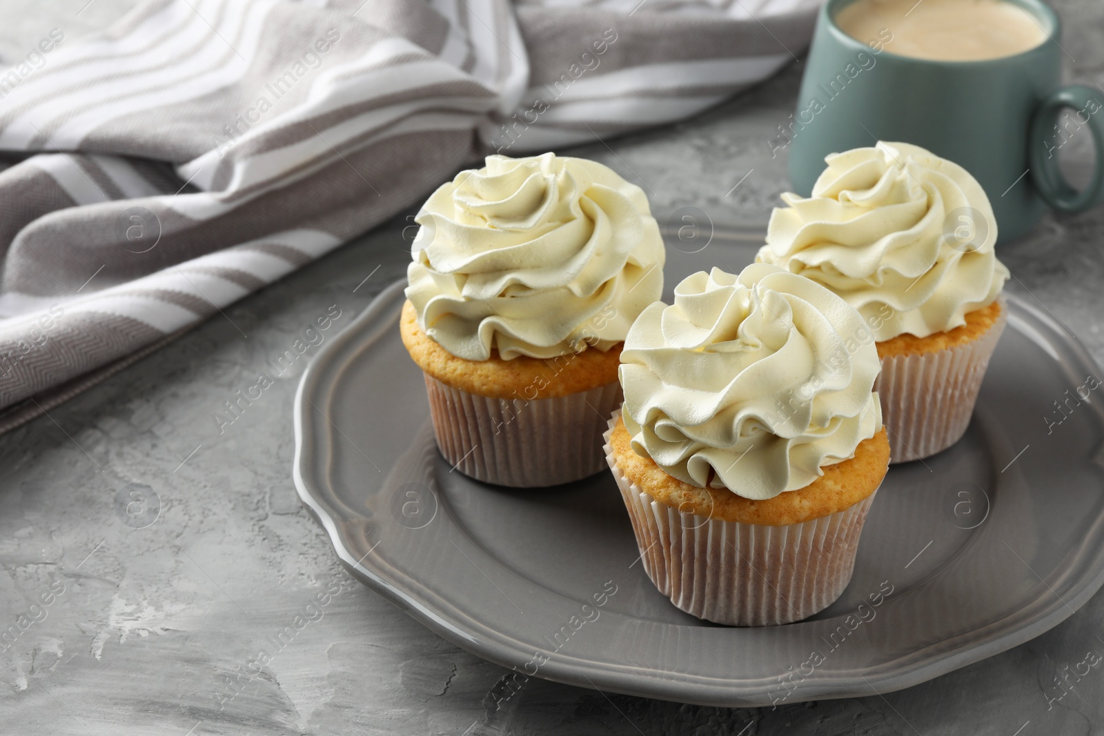 Photo of Tasty cupcakes with vanilla cream on grey table, closeup