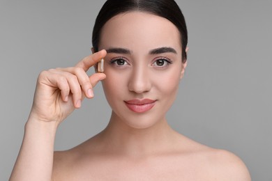 Beautiful young woman with vitamin pill on grey background