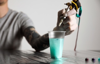 Photo of Tattoo artist cleaning machine needle at table, closeup