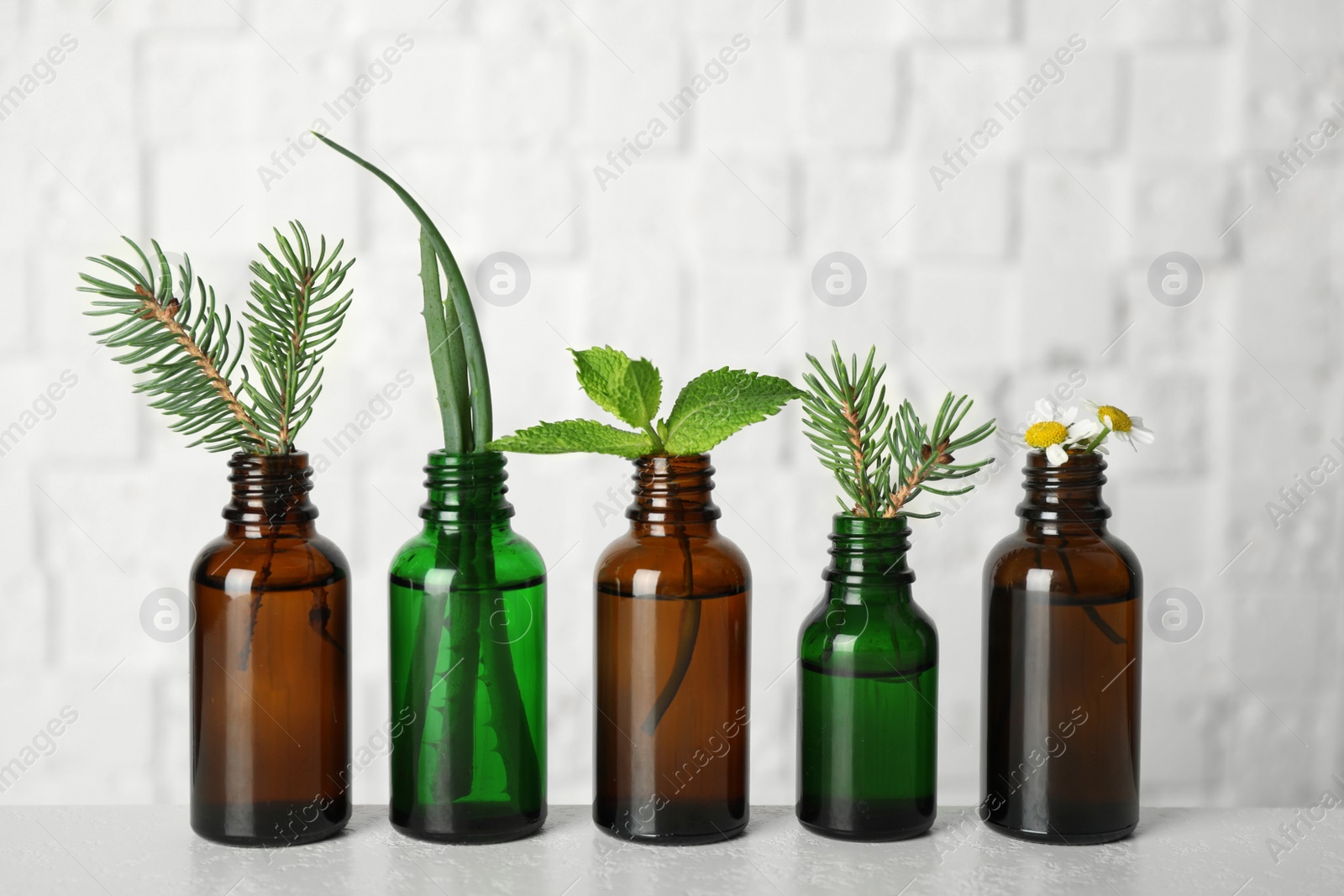 Photo of Glass bottles of different essential oils with plants on table