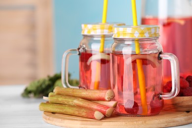Mason jars of tasty rhubarb cocktail with raspberry and stalks on white table. Space for text