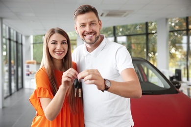 Photo of Happy man and woman with car keys in modern auto dealership