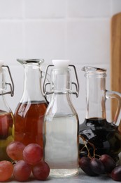 Photo of Different types of vinegar and grapes on grey table