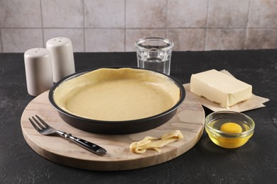 Photo of Pie tin with fresh dough and ingredients on black table. Making quiche