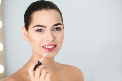 Photo of Young woman applying liquid lipstick on blurred background. Space for text