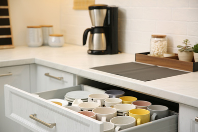 Photo of Open drawer with cups and coffeemaker on countertop in kitchen