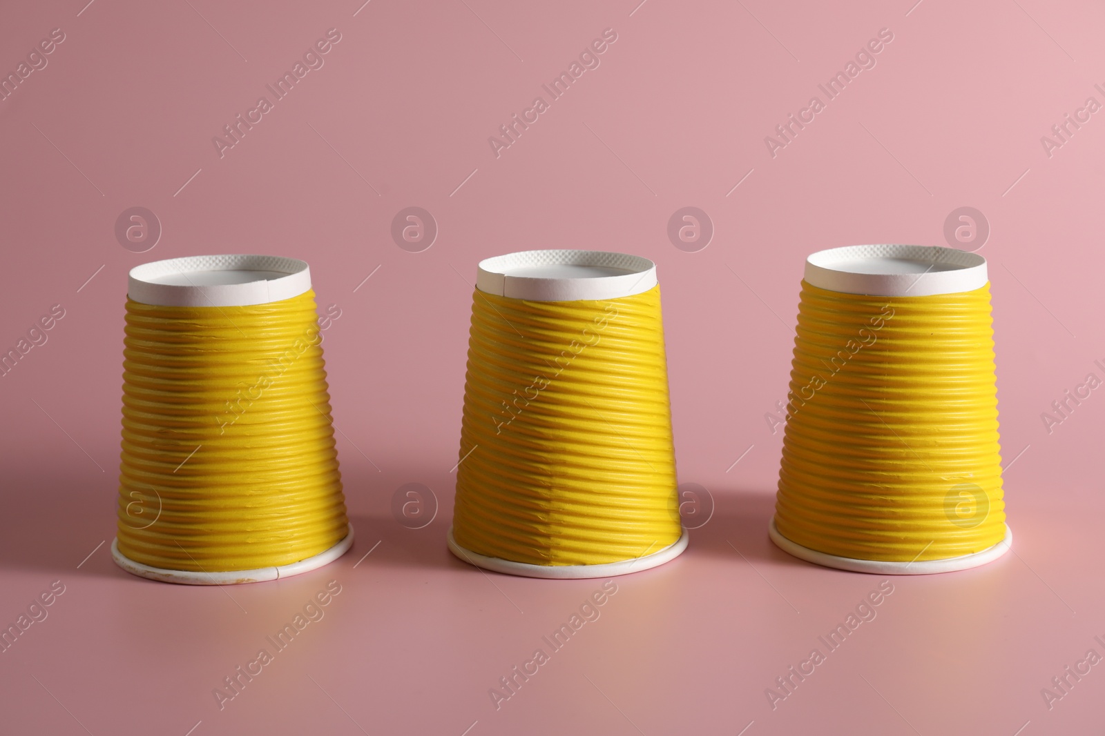 Photo of Shell game. Three yellow cups on pink background