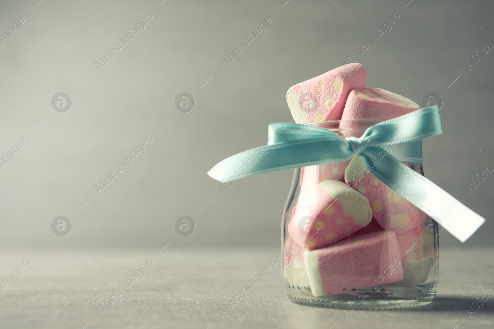 Photo of Tasty marshmallows in glass jar on light grey table, closeup. Space for text