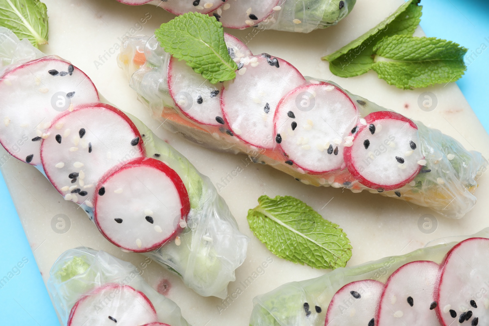 Photo of Delicious spring rolls and mint on light blue background, top view