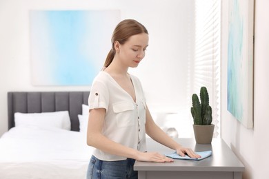 Photo of Woman with microfiber cloth cleaning grey chest of drawers in room
