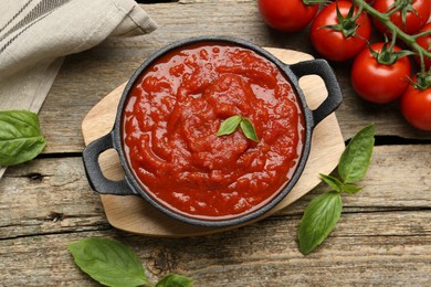 Photo of Homemade tomato sauce in bowl and fresh ingredients on wooden table, flat lay
