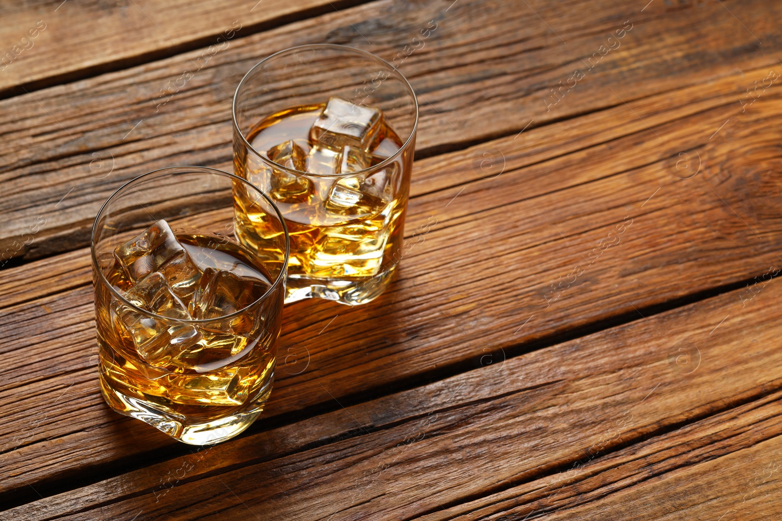 Photo of Whiskey with ice cubes in glasses on wooden table, space for text